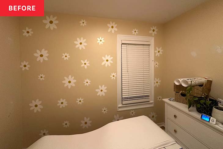A cozy bedroom with beige walls adorned with white daisies, a window with blinds, and a dresser topped with plants and storage baskets.