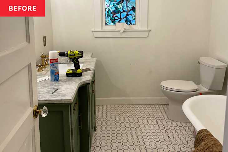 Bathroom with green vanity, marble countertop, drill, cleaning spray, and stained glass window. White toilet and hexagonal tile floor.