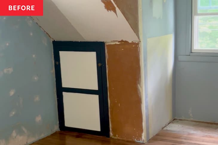 A corner of a room with unfinished walls, a dark blue cabinet door, and a window letting in natural light.