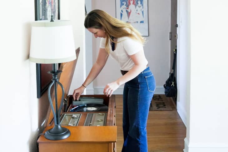 A woman putting on a record on a wooden turntable inside a bright apartment