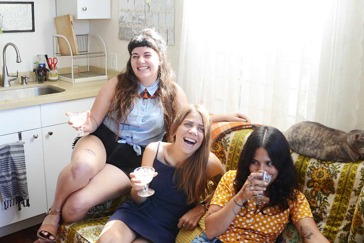 A group of three girlfriends laughing on the couch with cocktails