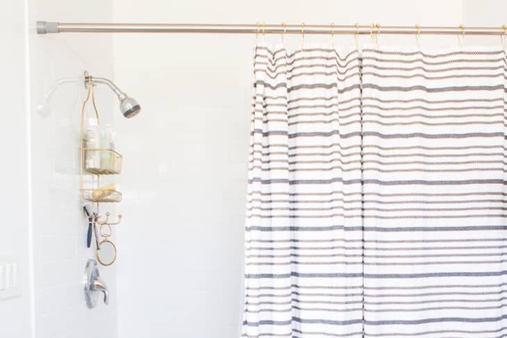 White shower with gold caddy and striped shower curtain