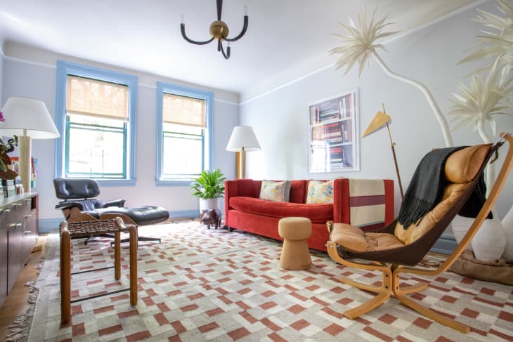 Living room with red sofa, patterned rug, leather lounge chair, and large windows with blue trim.