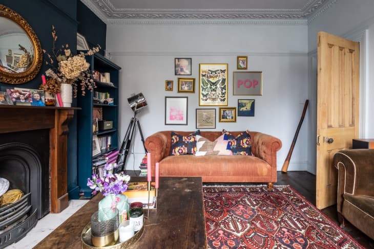 Living room with a brown sofa, colorful cushions, gallery wall, ornate fireplace, and a patterned red rug.