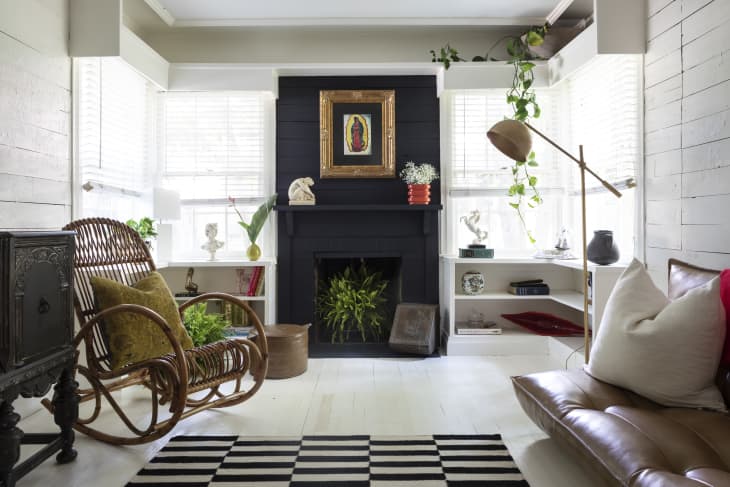 Cozy living room with a black fireplace, wicker chair, leather sofa, plants, and a striped rug.