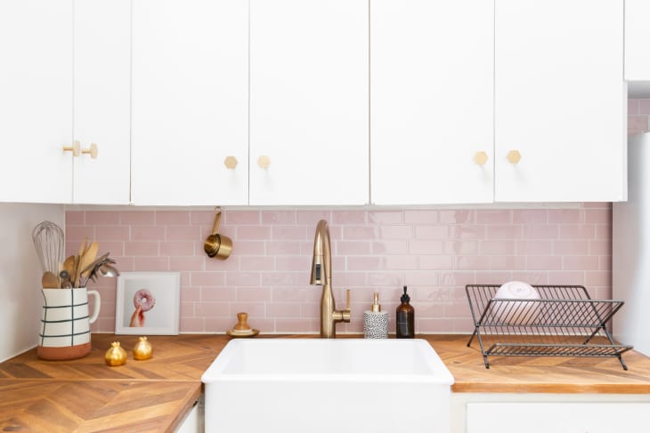 A small kitchen with a pink backsplash and a collapsible dish rack