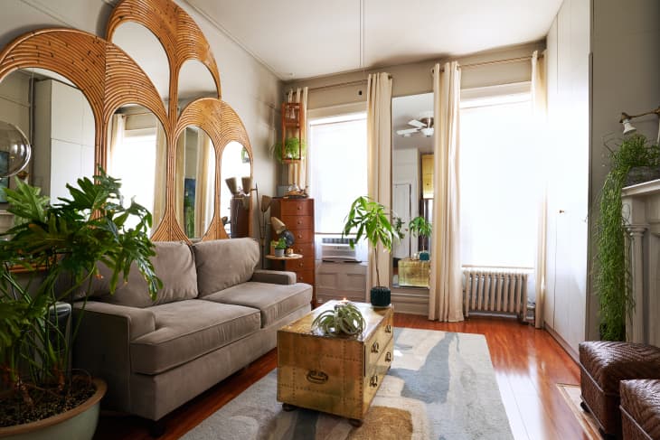 a brown and brass living room with green plants and a tall dresser in the corner