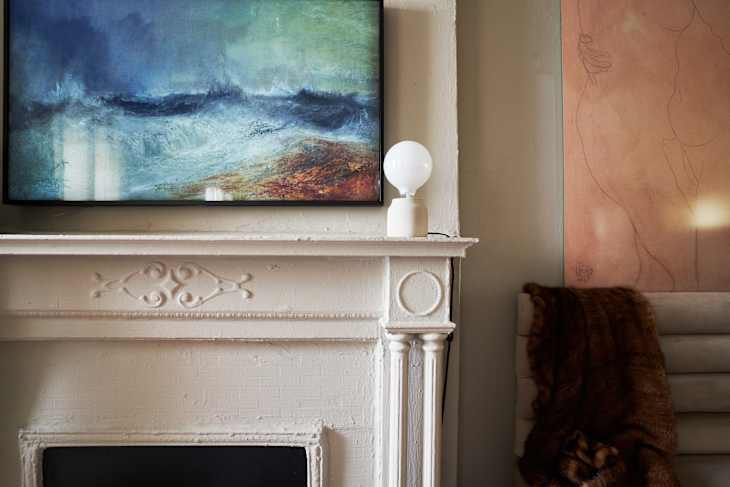 Painting of ocean waves above a white ornate fireplace with a round lamp.
