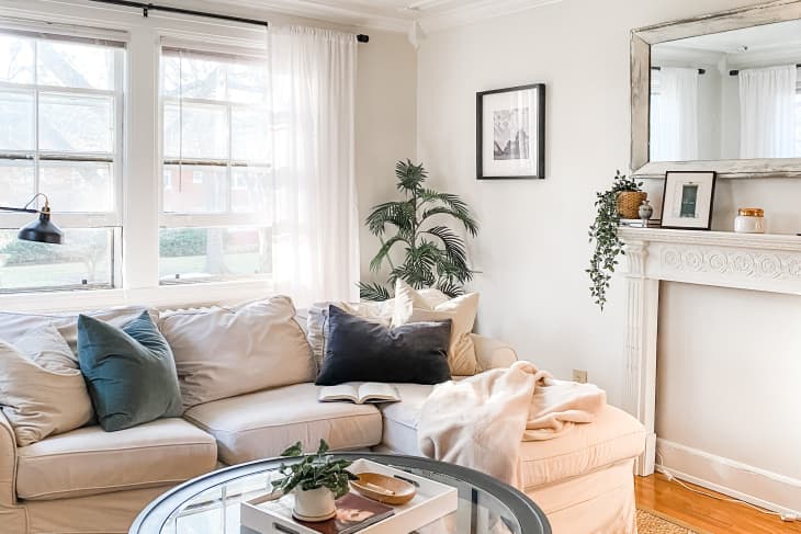 Cozy living room with a beige sectional sofa, green and black pillows, a round glass coffee table, and a decorated mantel.