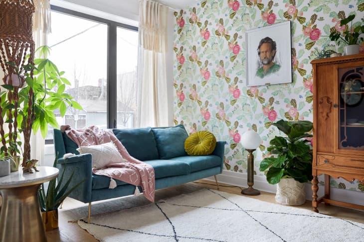Living room with blue sofa, floral wallpaper, wooden cabinet, plants, and a portrait on the wall.