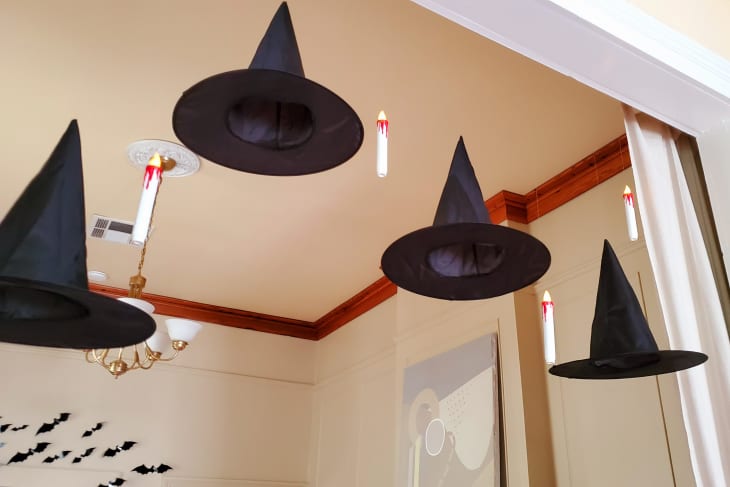 Floating witch hats and candles hang from the ceiling in a decorated room with bat decals on the wall.