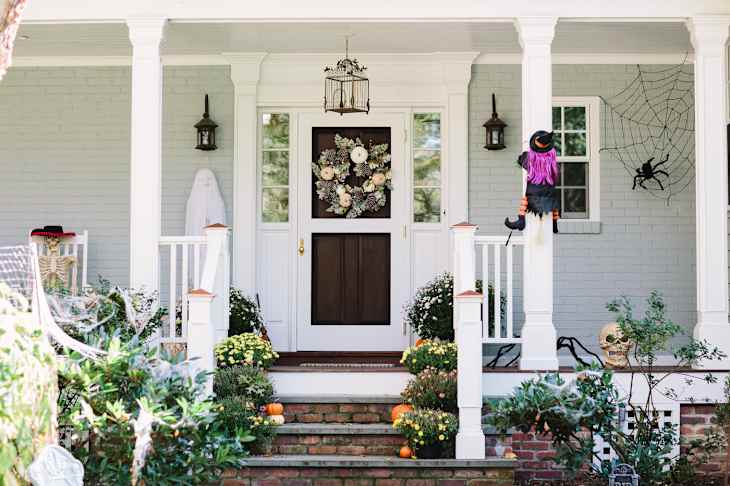 Front porch decorated for Halloween with a witch figure, skeleton, pumpkins, and a spider web.