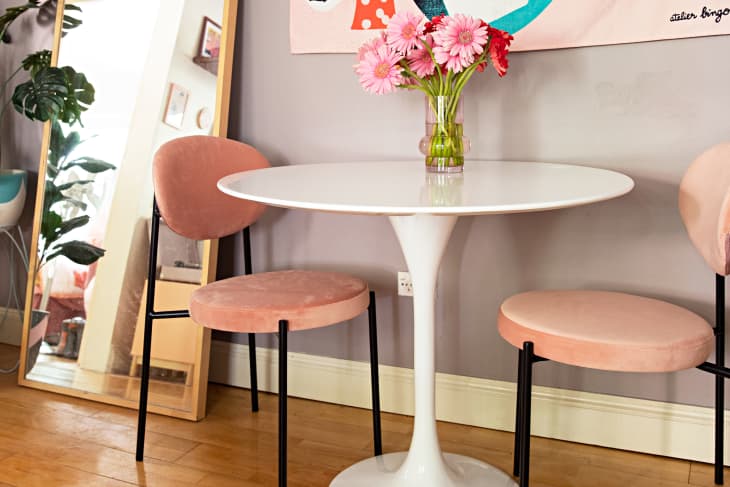Dining nook with small white tulip table, 2 pink chairs with black legs wood floor, vase of pink and red flowers, full length mirror on floor