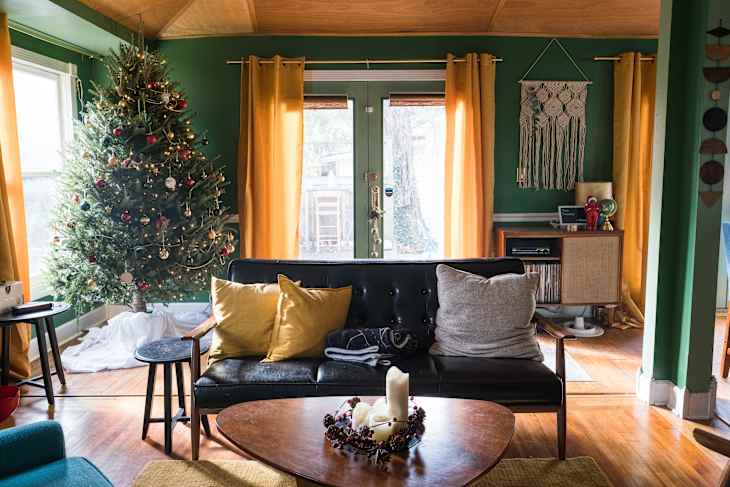 Living room with Christmas tree, black sofa, yellow curtains, and macramé wall hanging.