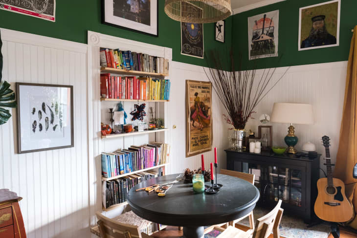 A room with white wainscoting, green upper walls, and a built-in bookshelf with books arranged by color