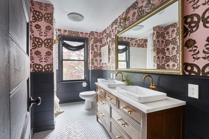 Bathroom with pink floral wallpaper, double sinks, gold faucets, large mirror, and hexagonal floor tiles.