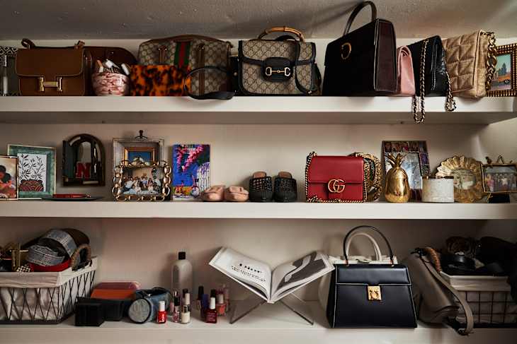 Shelves with designer handbags, framed photos, nail polish, and decorative items, including a gold pineapple and open book.