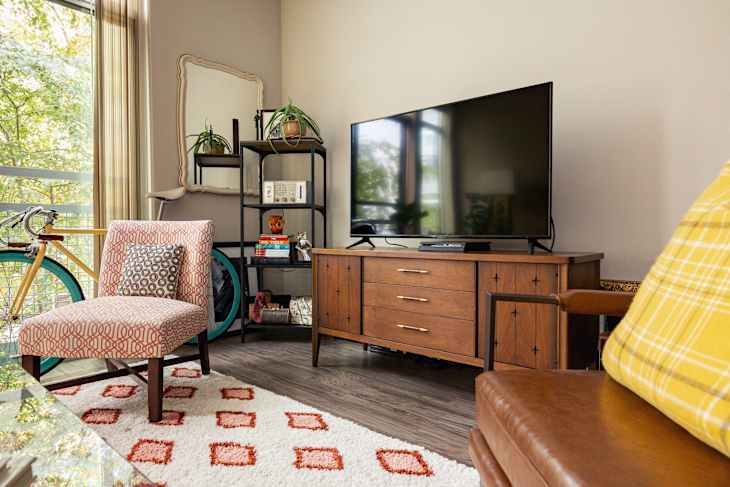 Living room with a patterned chair, wooden TV stand, large flat-screen TV, and a bicycle by the window.
