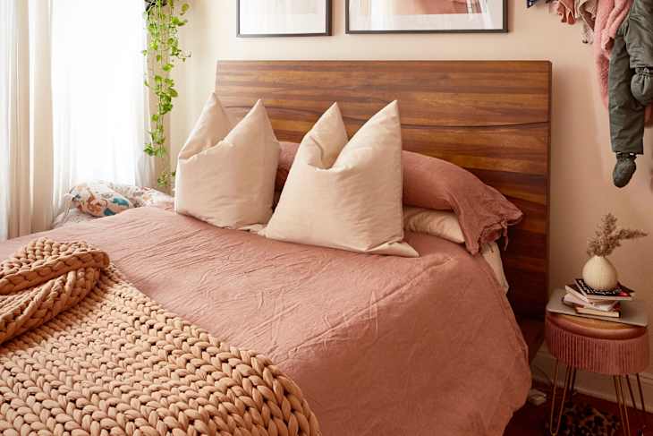 Cozy bedroom featuring a wooden headboard, pink bedding, large pillows, and a braided throw blanket.