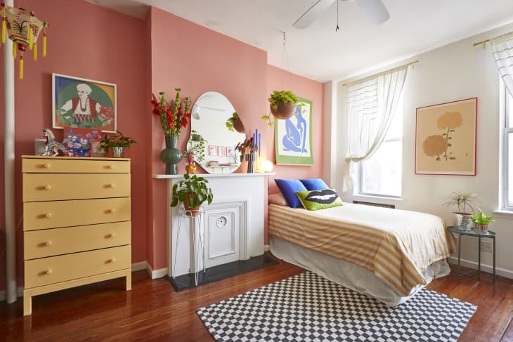 Bedroom with pink accent wall, yellow dresser, single bed, colorful pillows, and vibrant artwork.