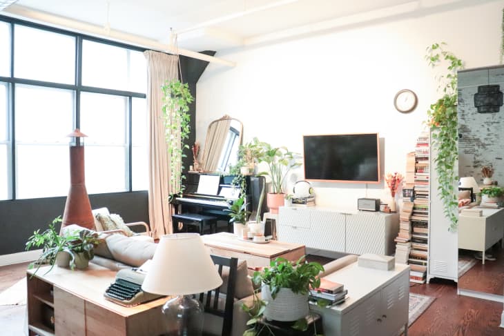 Living room with a piano, wall-mounted TV, bookshelves, plants, and a cozy sofa.