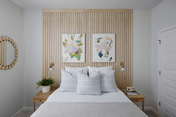 Bedroom with wooden slat accent wall, abstract art, white bedding, and bedside tables with lamps and decor.