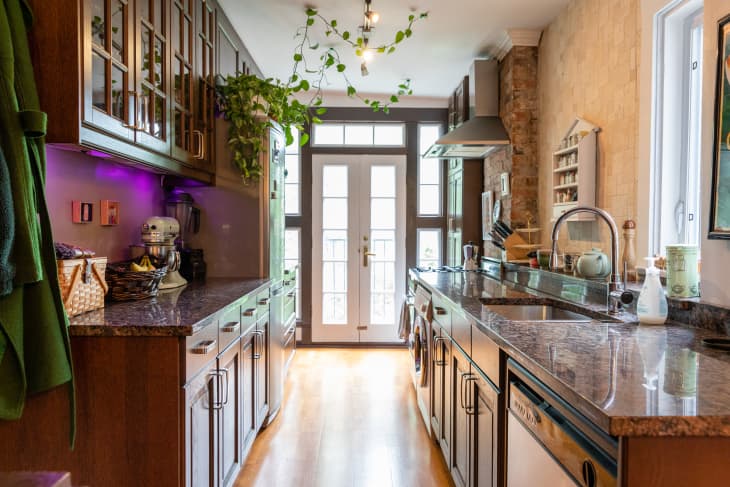 Galley kitchen with dark wood cabinets, granite countertops, hanging plants, and a mixer on the counter.