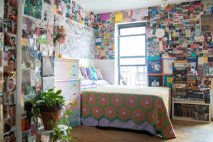 Bedroom with colorful collage walls, patterned bedspread, potted plant, and stacked board games by the window.