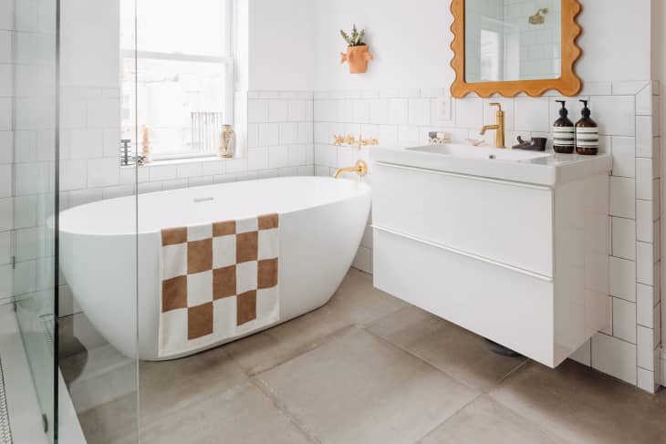 white bathroom with tiled walls, white freestanding tub, and brown and white checkered bath mat