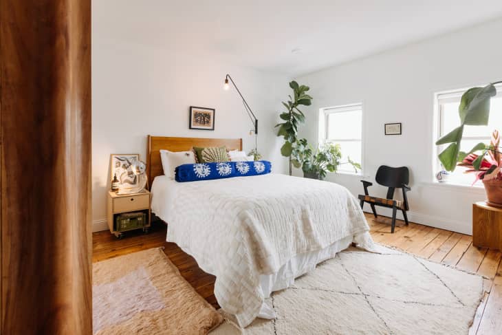 Philadelphia residence with white walls, lots of wood details: bedroom with bed with wood headboard, white linens, blue and green pillows. Lots of plants, 2 shag area rugs