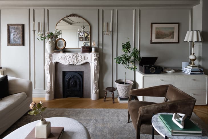 White fireplace, brown sueded armchair and white dresser in neutral colored living room
