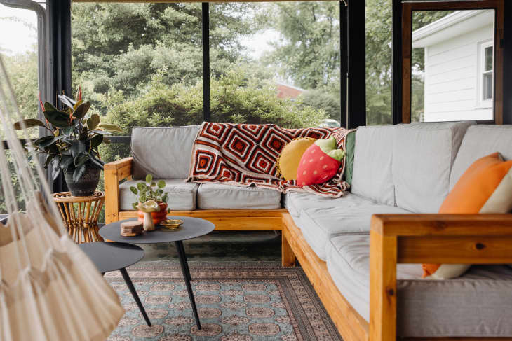 Grey outdoor sectional topped with blankets and decorative pillow in enclosed patio.