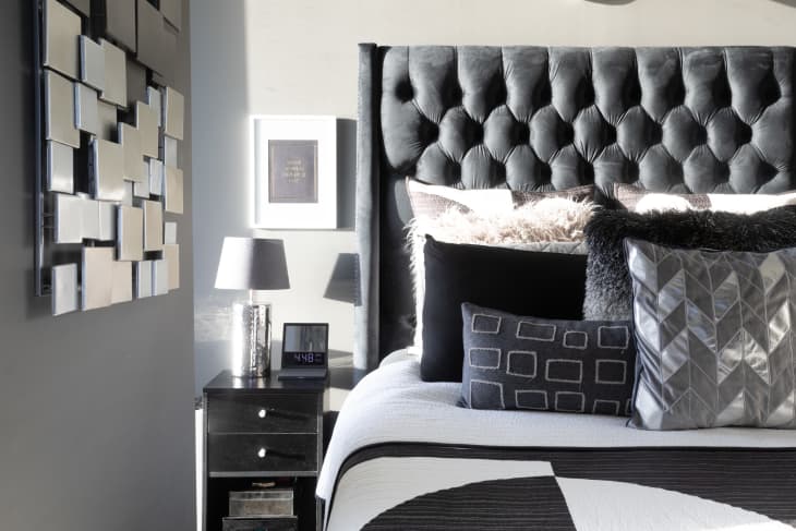 Bedroom with lots of black, white, and gray. Graphic geometric linens, throw pillows. Tufted gray headboard