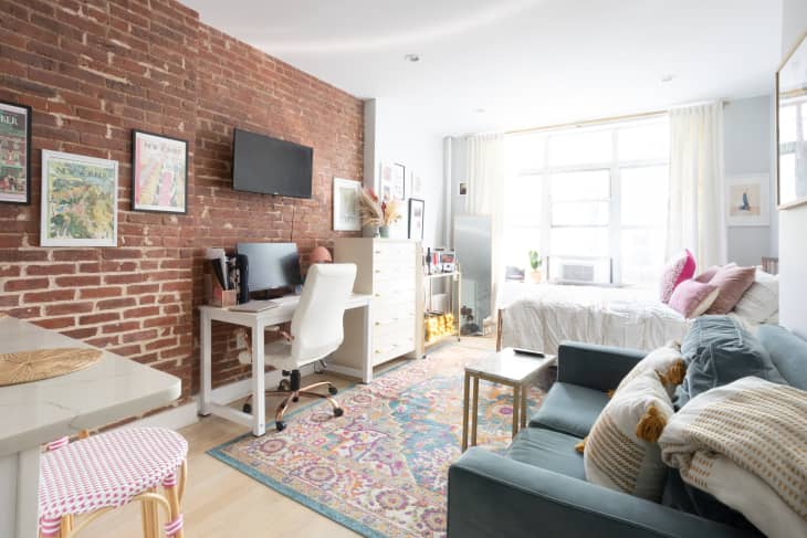 Studio apartment in New York City with bedroom, small sofa and white desk.