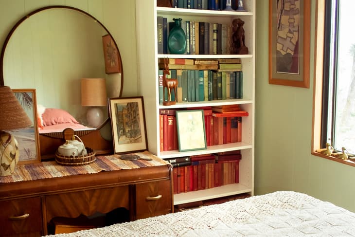 pale green bedroom with white bookshelves and vintage wood vanity table with round mirror