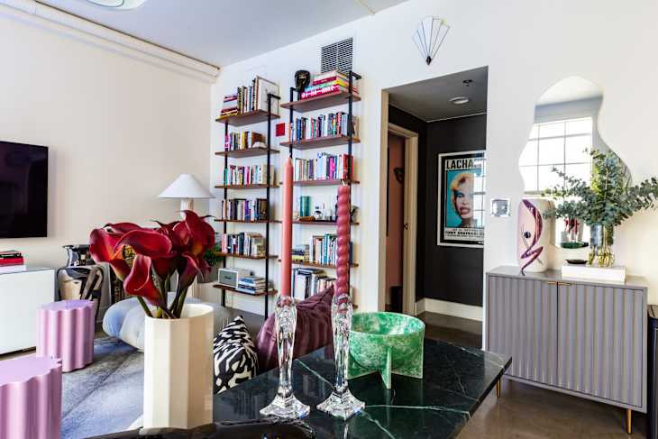 living room with pale gray floor sectional with black and white throw pillows, 2 small lilac wavy tables, large paned windows, potted tree, gray area rug