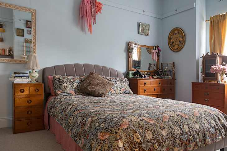 A bed with floral sheets and wooden bedroom furniture.