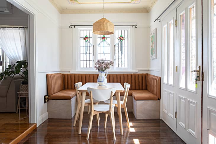 A breakfast nook surrounds a dining table with three chairs in a white kitchen with decorative wall dressings.