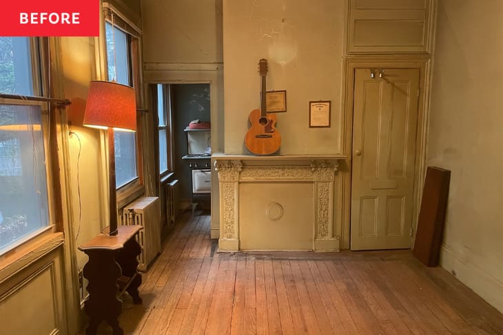 Sealed fireplace, guitar on mantle, lamp table, wood floors, dirty doors and paneling