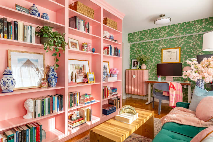 A living room with a green fabric couch across from a pink bookcase and gallery wall