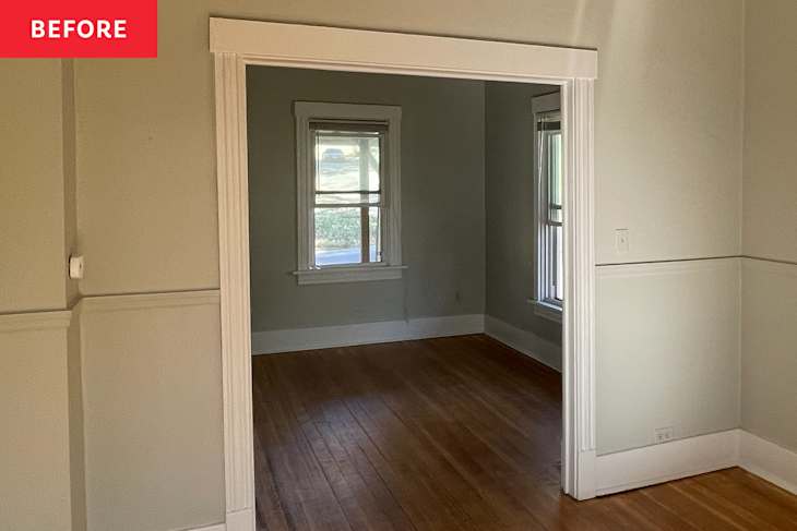 Empty room with hardwood floors, light green walls, and two windows, viewed through an open doorway.
