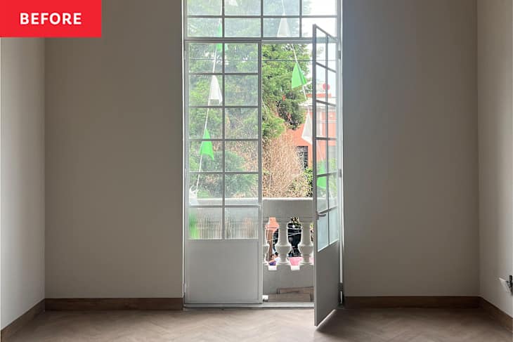 Empty room with a large window and open door leading to a balcony, featuring green decorations outside.