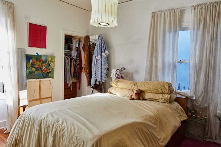 Cozy bedroom with a large bed topped with yellow bedding, a teddy bear, and a colorful painting on the wall.