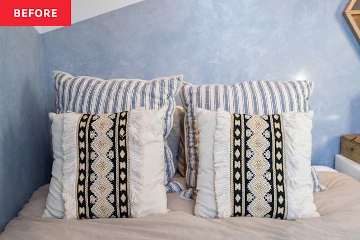 Two decorative pillows on a bed, featuring striped and patterned designs, against a blue wall.