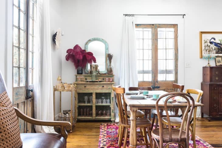 Dining room with wooden table, mixed chairs, vintage cabinet, red feather decor, and colorful rug.