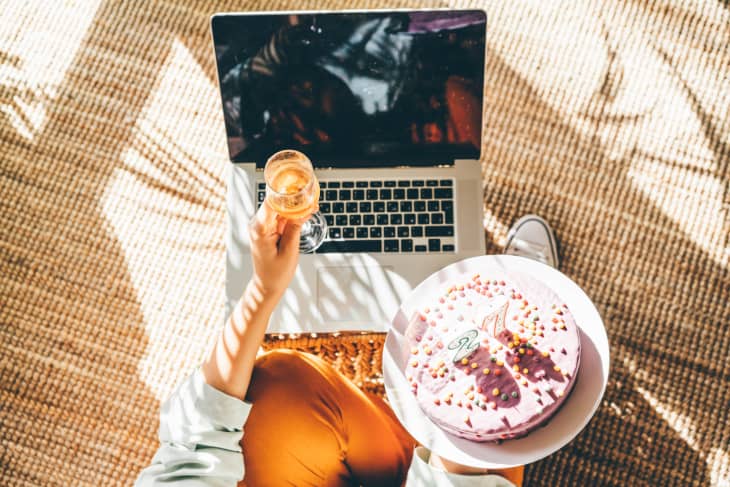 Woman blowing out the candle on the birthday cake and making video call. Girl celebrating birthday online in quarantine time. Close up birthday cake and laptop.