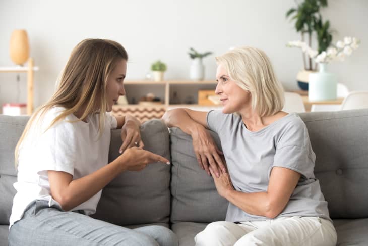 Middle aged woman sitting on sofa in living room with millennial female communicating at home