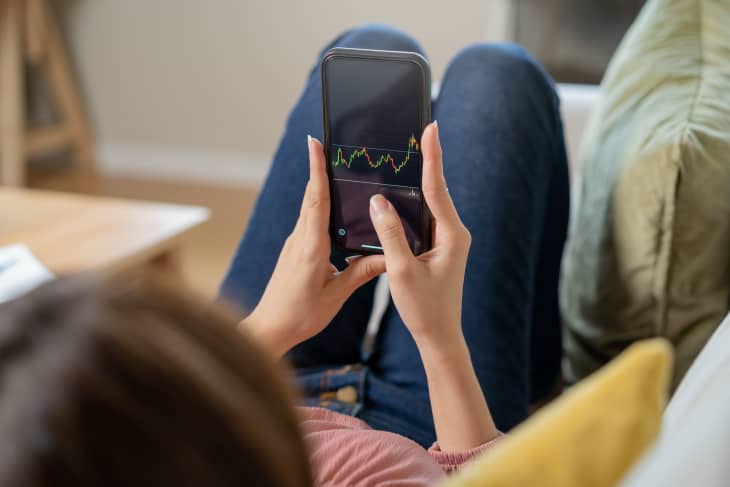 Woman on couch holding phone analyzing stock market