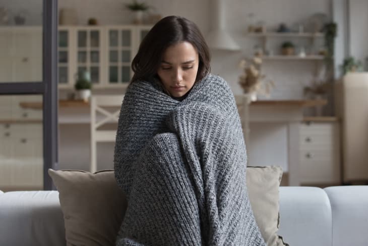 Woman sitting on couch wrapped in blanket looking sad