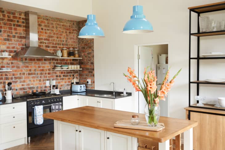 Kitchen with wooden kitchen island, blue pendant lights, and exposed brick wall